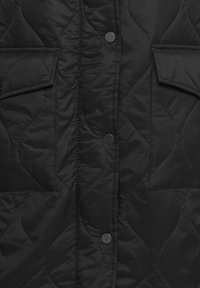 Chaqueta negra acolchada con dos bolsillos frontales, botones a presión y una textura suave y brillante. Presenta un patrón de costuras onduladas.