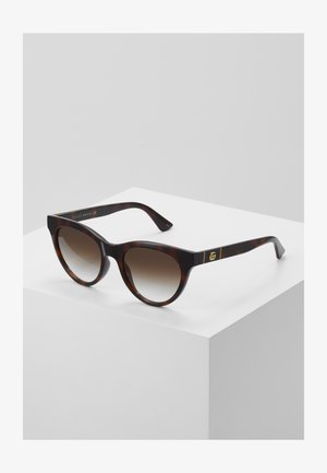 Schildpatt-Sonnenbrille mit Katzenaugenform, verlaufenden braunen Gläsern, goldenen Logoakzenten auf den Bügeln, eleganter, glänzender Oberfläche.