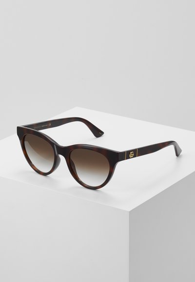 Tortoiseshell sunglasses with a cat-eye shape, gradient brown lenses, gold logo accents on the arms, sleek, glossy finish.