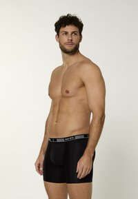 Boxer in microfibra nera con un elastico bianco e nero che riporta il nome del brand. Design aderente, lunghezza a metà coscia.