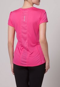 Camisa atlética ajustada en un brillante color rosa, con mangas cortas, detalles de malla en la espalda y acentos reflectantes a lo largo de la columna.