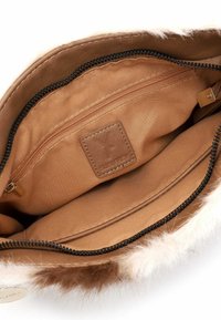 Interno di una borsa in finta pelliccia marrone con rivestimento in tessuto beige, tasca con zip e etichetta del marchio. Cucitura decorativa lungo la cerniera.