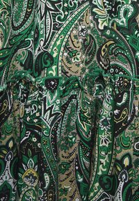 Zelená látka s vzorem paisley a složitými designy v různých odstínech zelené, černé a žluté. Má skladaný lem a texturovaný potisk.