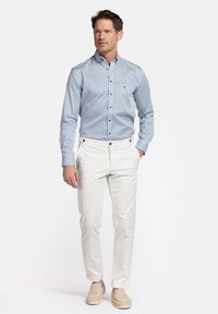 Chemise boutonnée bleu clair avec un motif géométrique, associée à un pantalon blanc et des chaussures slip-on beiges.