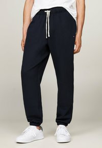 Marineblaue Sweatpants aus einem Baumwoll-Mix mit elastischen Bündchen, verstellbarem Bund und Seitentaschen; kombiniert mit weißen Turnschuhen.