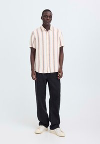 Korte mouwen, gestreept overhemd in pasteltinten; voorzien van knopen en een kraag. Gecombineerd met zwarte wijde broekspijpen en lichtgekleurde sneakers.