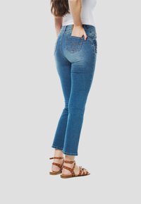 Blauwe spijkerbroek met een aansluitend ontwerp, mid-rise taille en iets uitlopende pijpen. Gecombineerd met bruine sandalen met studs.