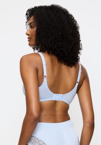 Vaaleansininen rintaliivit, joissa säädettävät hihnat, sileä pinta ja takana hakaskiinnitys. Sivulla näkyy pitsikoristelu.