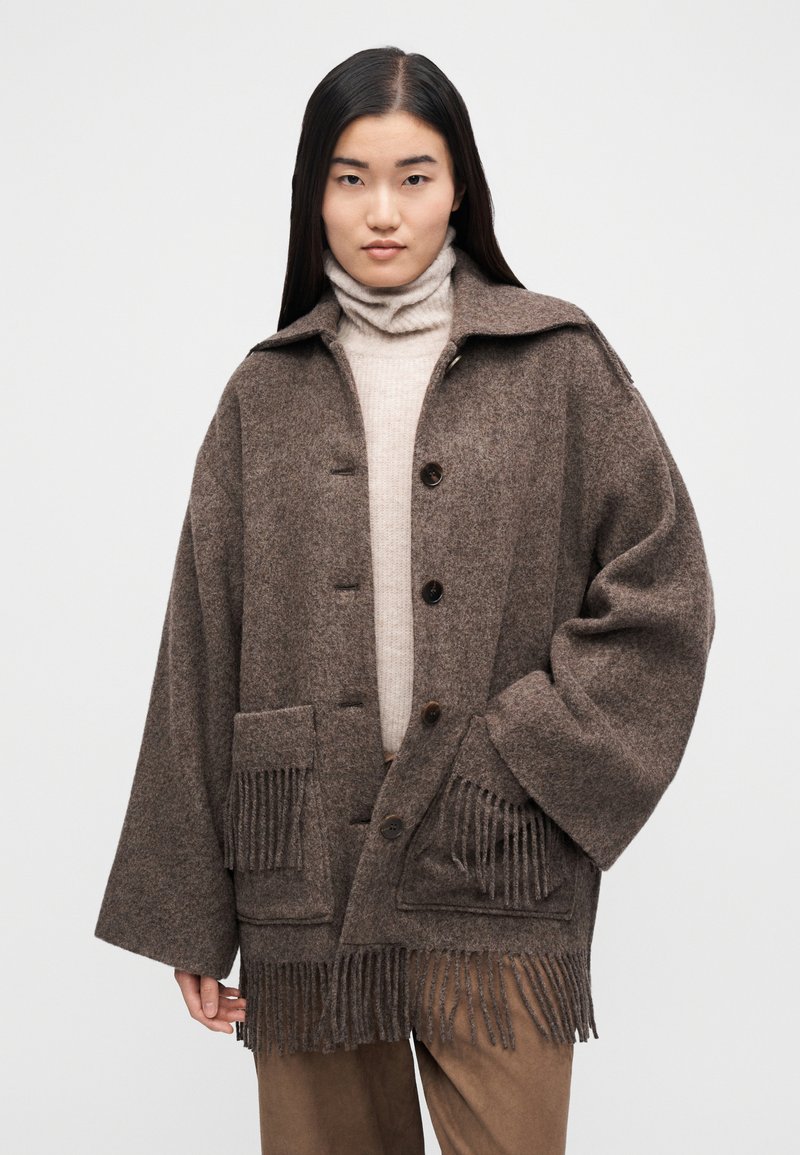 Brun frakk i uldblanding med oversized pasform, krave, forlommer og frynsekant i kanten. Har knapper og en afslappet pasform. Struktureret stof.