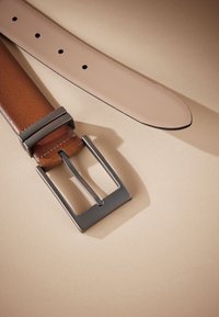 Cintura in pelle marrone con superficie liscia, dotata di fibbia rettangolare argentata. La cinghia presenta diversi fori e bordi lisci.