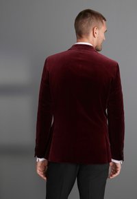 Bordo aksominis švarkas su pritaikytu siluetu, išpjautomis atlapomis, šoninėmis angomis ir juodais mygtukais. Lygus paviršius, derinamas su juodomis kelnėmis.