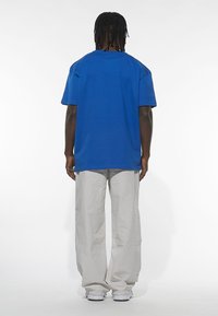 T-shirt blu in cotone con maniche corte e vestibilità rilassata, abbinato a pantaloni grigi chiari svasati, realizzati in materiale testurizzato.
