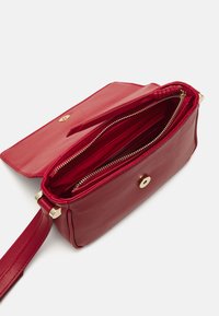 Borsa a mano in pelle rossa con hardware dorato, dotata di un compartimento con zip e una tasca interna. La borsa ha una texture liscia e una forma strutturata.