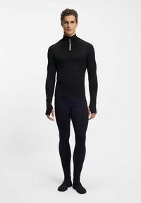 Czarna bluzka z długim rękawem, wysokim kołnierzem i suwakiem na ćwierć długości, w połączeniu z czarnymi dopasowanymi legginsami. Gładka tekstura i elastyczna tkanina.