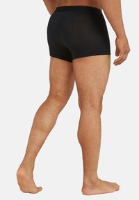 Černé boxerky vyrobené z hladkého, pružného materiálu, s jednoduchým páskem. Pohled ukazuje zádovou a boční část šortek a nohou.