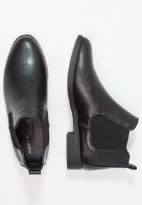 Botas de cuero negras hasta el tobillo con paneles laterales elásticos, un tacón texturizado y un acabado suave. Inscritas con "ANNA FIELD" en la plantilla.