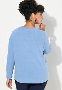 Maglietta a maniche lunghe di un soffice blu, con scollatura rotonda e spacchi laterali, abbinata a pantaloni scuri. Il tessuto sembra strutturato e leggero.