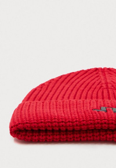 Rode geribbelde gebreide muts met een omgeslagen rand en een minimalistisch zwart logo accent. Zachte textuur met een aansluitende vorm.