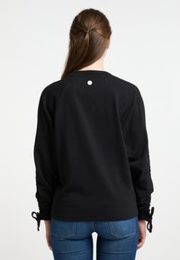 Felpa nera con maniche raglan, dettagli arricciati ai polsini e scollatura rotonda. Tessuto liscio con un piccolo logo sul retro.