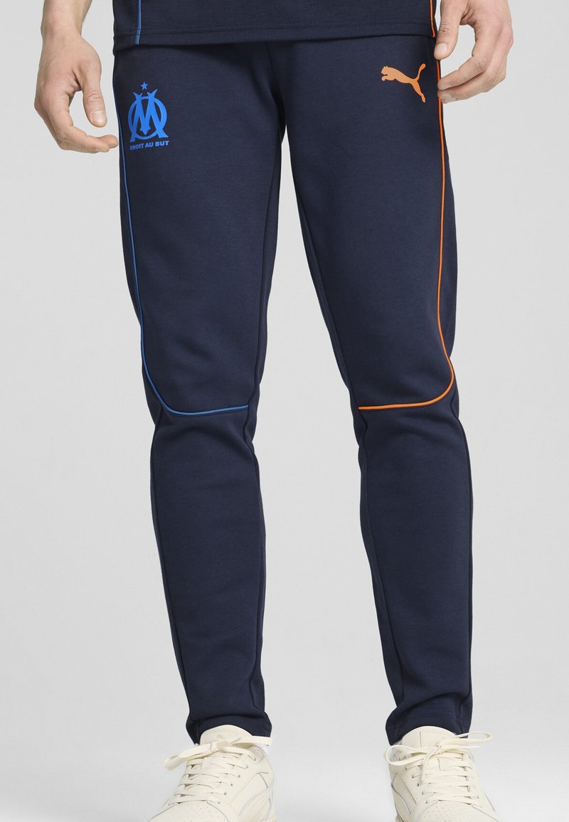 Jūržvalgos sportiniai džinsai su pritaikyta forma, mėlynos ir oranžinės spalvos šoninėmis detalėmis bei Marseilio logo. Pagaminti iš minkštos medžiagos, turi elastingas rankoves.