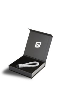 Braided gray silicone bracelet with a black clasp, presented in a black box with a logo on the inside lid. Soft texture, minimal design.