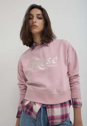 Light pink sweatshirt with "Rosé Lovers" in metallic silver font, paired with a checkered pink and white flannel shirt underneath.