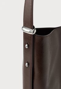 Saco tote de couro castanho com uma textura suave, ferragens prateadas e uma única alça presa com rebites e um fecho polido.