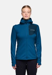 Blauwe jas met ritssluiting, capuchon en een zwart borstzakje. Voorzien van lange mouwen en duimgaten, gemaakt van een gladde, rekbare stof.