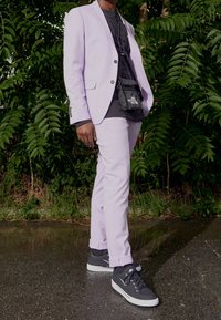 Lila kostym med en figursydd kavaj och smala byxor, bärs över en svart t-shirt. Matcher med svarta sneakers med vita sulor.