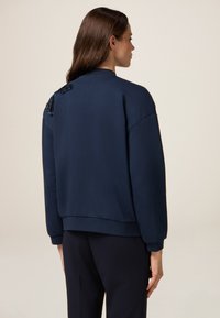 Sudadera azul marino de corte relajado, con un detalle de lentejuelas texturizadas en la parte posterior y puños y dobladillo acanalados. Tejido suave.