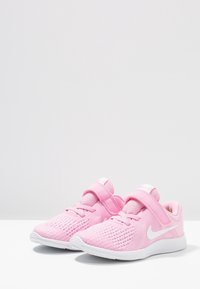 Růžové sportovní boty s vrchní částí z prodyšné síťoviny a textilu, s bílým logem Nike Swoosh, zapínáním na pásek, texturovanými vzory a lehkou bílou podrážkou.