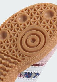 Suola della scarpa con una superficie in gomma strutturata e decorata di colore marrone chiaro, con disegni circolari e triangolari; tomaia in tessuto rosa visibile.