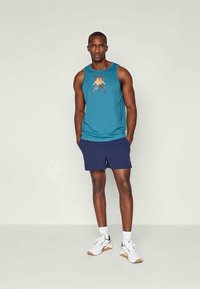 Blå tanktopp med en oransje logo, sammen med mørk marineblå shorts. Fullfører antrekket hvite joggesko med mørke aksenter.