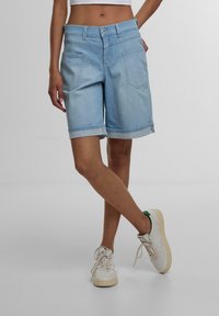 Shorts en jean bleu clair avec un ourlet retroussé, présentant des poches avant et arrière, une fermeture à bouton et une coupe droite.