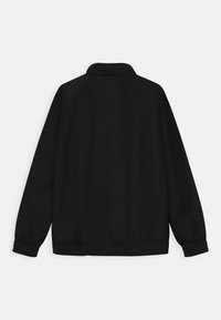 Chaqueta negra con cuello, puños y dobladillo elásticos. Textura lisa, material ligero y sin logotipos ni patrones visibles.