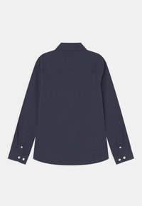 Achteraanzicht van een donkerblauwe blouse met lange mouwen, met knoopmanchetten en een klassieke kraag, op een witte achtergrond.