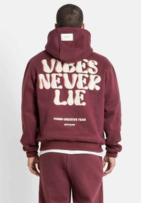 Felpa con cappuccio color bordeaux con ampio testo bianco "VIBES NEVER LIE" sul retro, polsini e orlo a coste, realizzata in tessuto morbido.