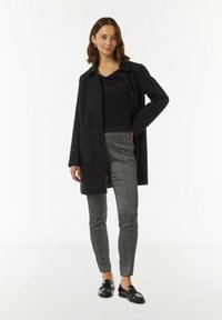 Czarny teksturowany płaszcz z kołnierzem, połączony z spodniami w czarno-białą kratę. Czarne lakierowane mokasyny dopełniają wygląd.