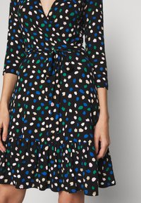 Svart klänning med en invecklad design, trekvartsärmar och en volangkant. Har ett flerfärgat stänk-mönster i rosa, grönt och blått.