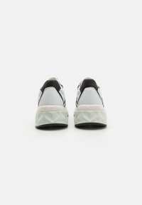 Hvit og svart sneaker med en teksturert såle, fremtredende merkevarelogo på hælen, og et strømlinjeformet, moderne design.