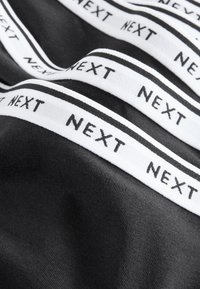 Tissu noir avec des bandes blanches portant le texte "NEXT", texture lisse et finition douce. Les bandes présentent des rayures noires altern�ées le long des bords.