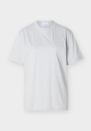 Λευκό κοντομάνικο T-shirt με στρογγυλή λαιμόκοψη και υφασμάτινο έμβλημα λογότυπου Lacoste στην αριστερή πλευρά του στήθους, καθώς και ετικέτα στο εσωτερικό του γιακά.