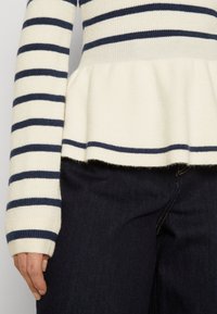 Pull en tricot rayé crème et marine, avec une conception à volant et une texture côtelée, associé à un jean en denim foncé.