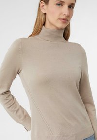 Beżowy sweter z golfem w żebrowanym wzorze. Posiada dopasowane rękawy oraz subtelne skośne przeszycia po bokach. Miękka struktura.