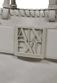 Borsa a tracolla grigia chiara con texture intrecciata, con un pannello rettangolare che riporta il logo "Armani Exchange" in una tonalità coordinata.