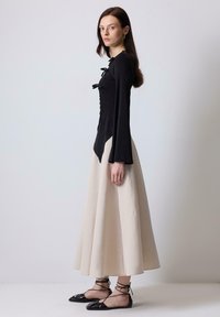 Top nero a maniche lunghe con dettagli arricciati e lacci, abbinato a una gonna fluida color crema. Scarpe basse nere con lacci avvolgenti.