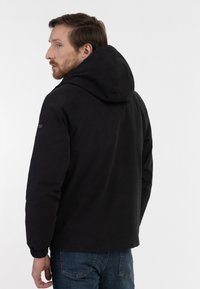Sort hættejakke med mat finish, der har elastiske manchetter og en glat tekstur, i en afslappet pasform med minimal detaljering.