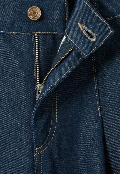 Jeans de denim de color azul oscuro, con un zipper metálico, botón dorado y costuras en contraste en los bolsillos y la cinturilla.