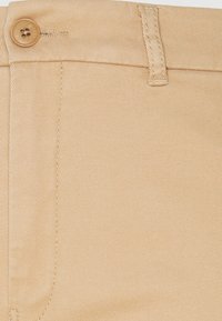 Beige twillbyxor har en knappstängning, smal midja och diagonala sömmar. Tyget har en slät textur.