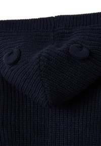 Dunkelblaues gestricktes Kleidungsstück mit einer gerippten Textur, zwei dekorativen Knöpfen und einem geformten Kragen am oberen Rand.
